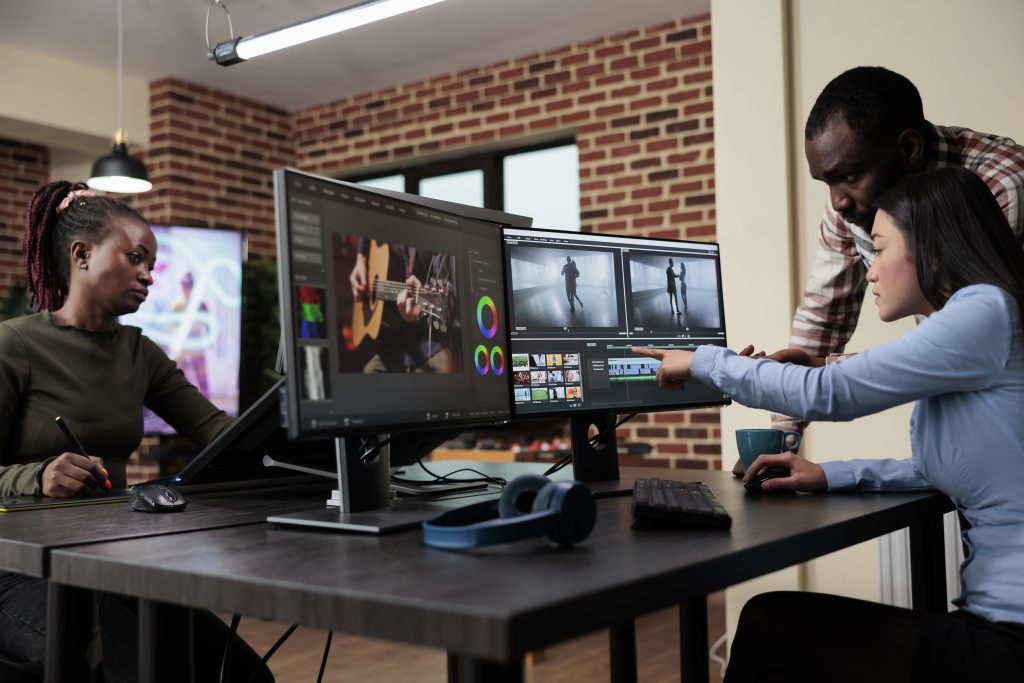 professional videographer sitting at desk while coworker helping her with film footage visual quality improvement.